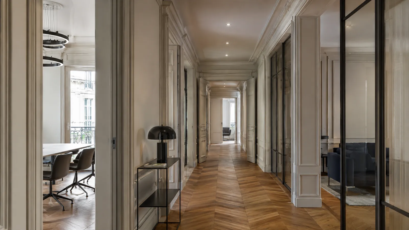 Couloir d’un immeuble haussmannien rénové : parquet ancien à chevrons, moulures préservées et cloisons vitrées